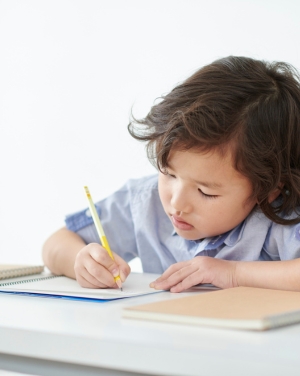 Jong kind met donkerbruin haar schrijft aan tafel in een schrift