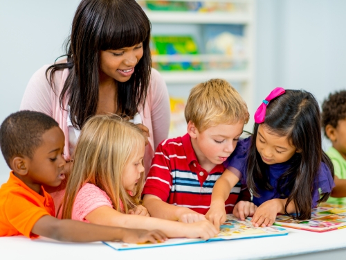 Leraar observeert jonge kinderen die aan tafel een boek lezen